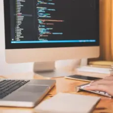 Code auf Monitor mit Laptop und Notizen – technische Umsetzung bei der Webseiten-Erstellung.